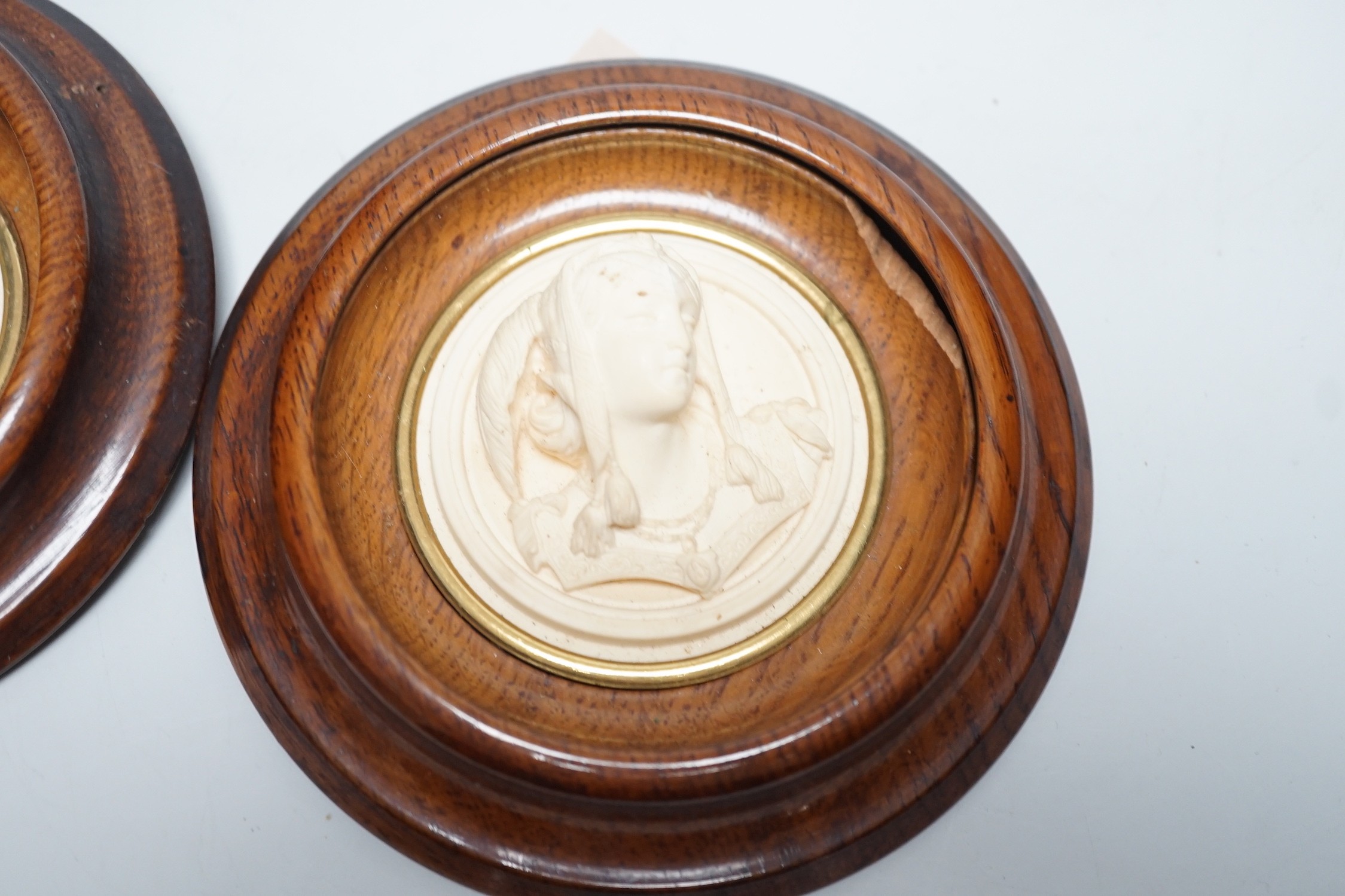 A pair of late 19th century carved and moulded composition portrait roundels, in oak frames